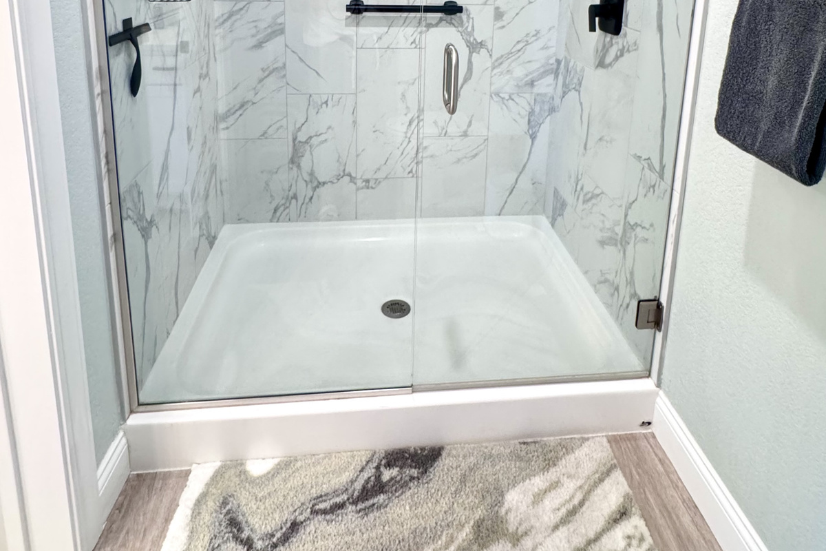 Primary Shower has a large walk-in shower with a safety bar, glass doors, a removable hand wand, and toiletries.