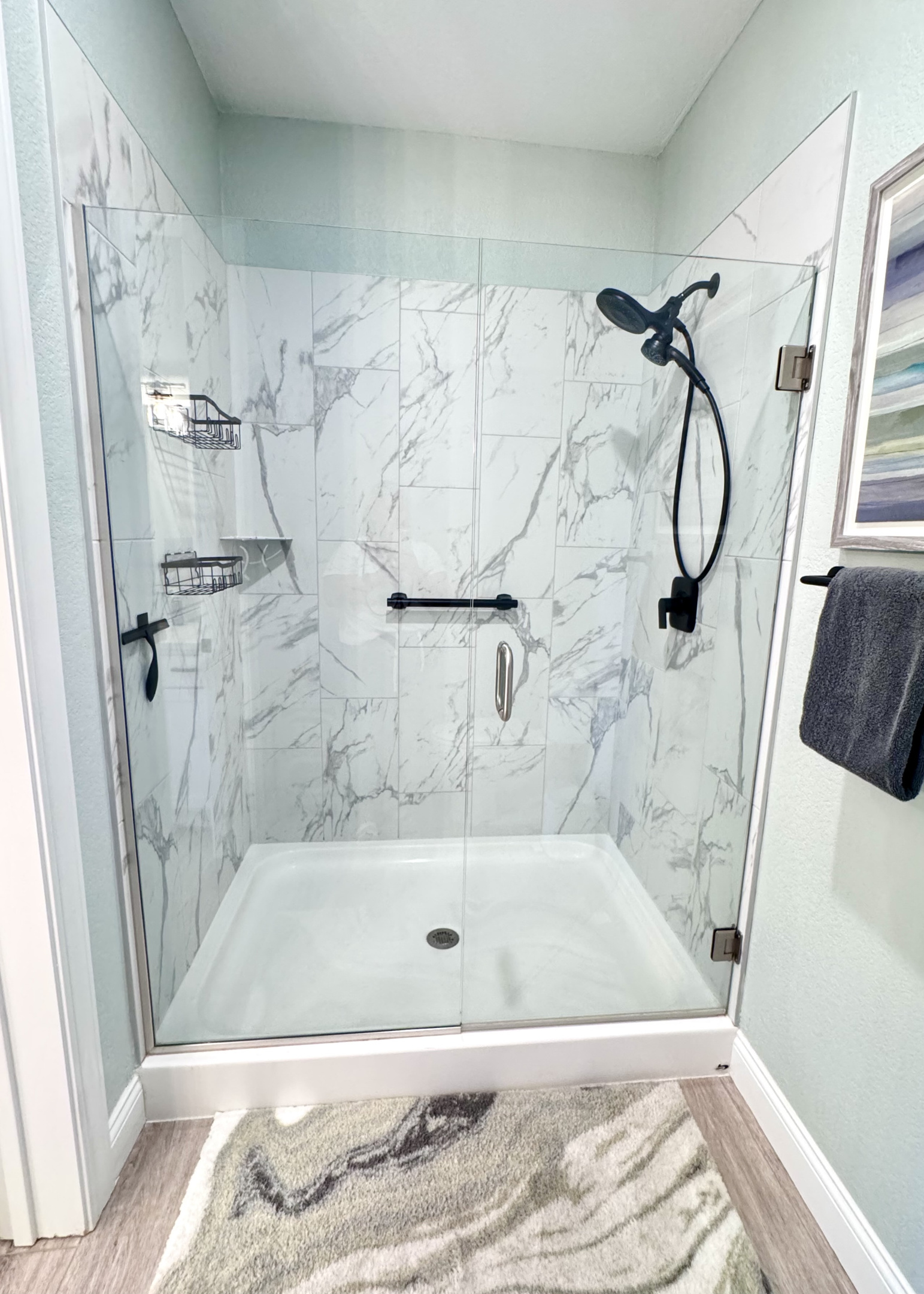 Primary Shower has a large walk-in shower with a safety bar, glass doors, a removable hand wand, and toiletries.
