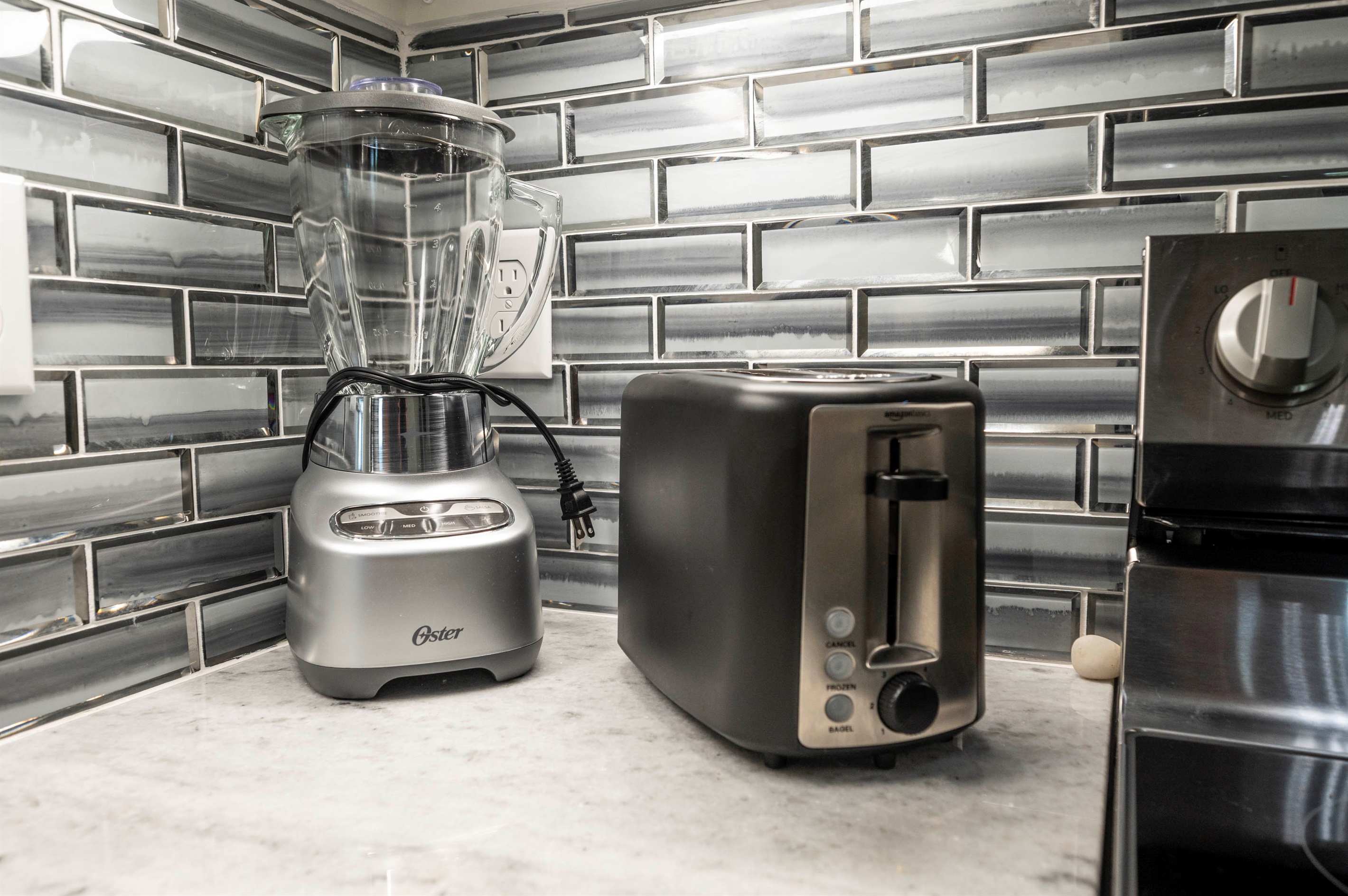 Sleek kitchen corner with modern toaster, blender, and glossy tile backsplash.
