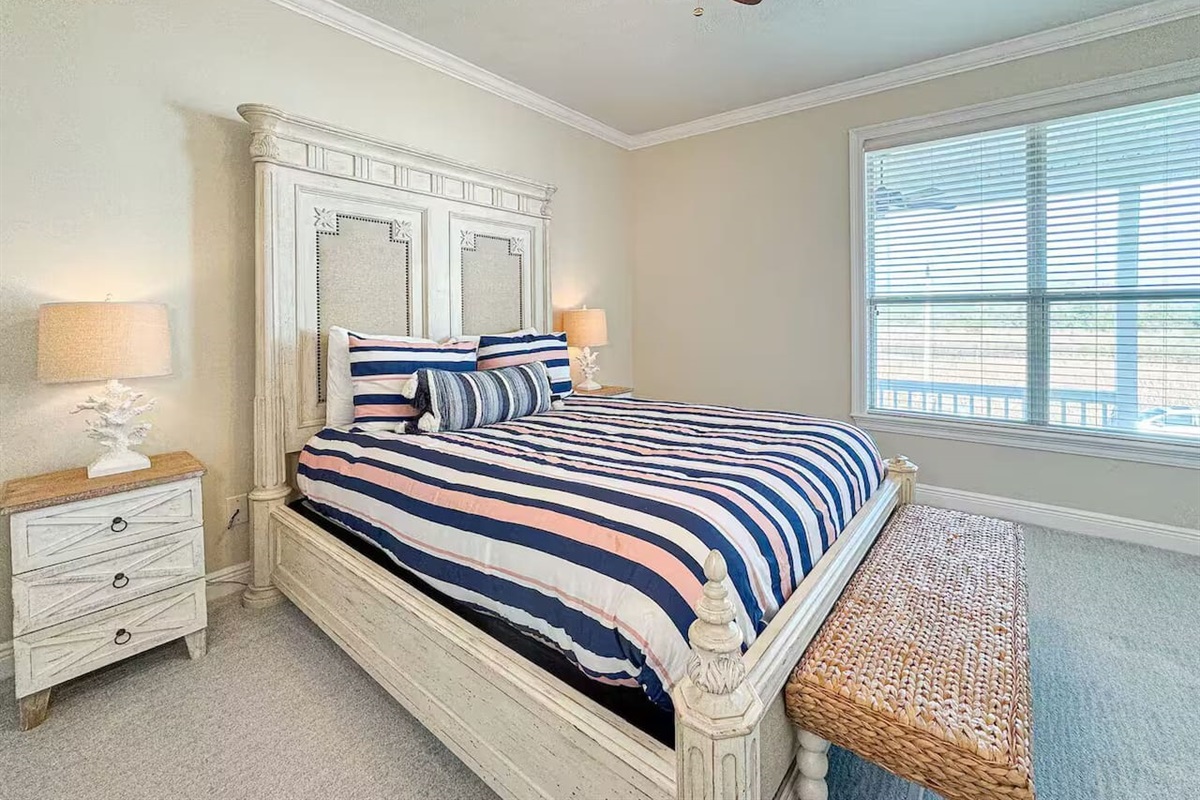 Spacious bedroom with a comfortable bed, fresh linens, and warm lighting. Includes bedside tables, ceiling fan, and cozy seating for a relaxing stay.