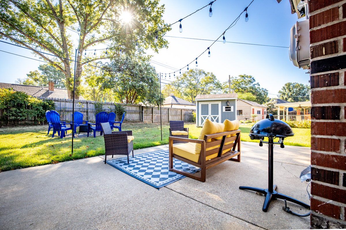 Fenced backyard with string-lit patio, fire pit, and electric grill.