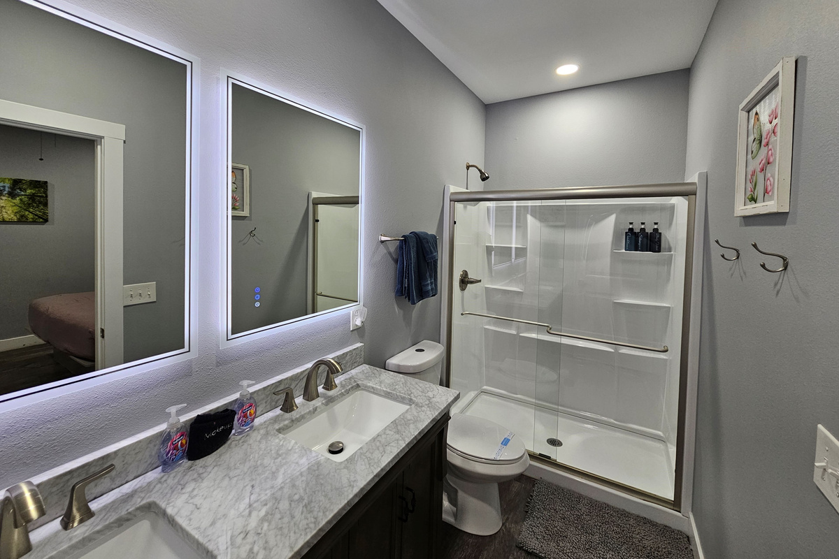 Clean and inviting bathroom with walk in shower, backlit mirrors, & fresh linens
