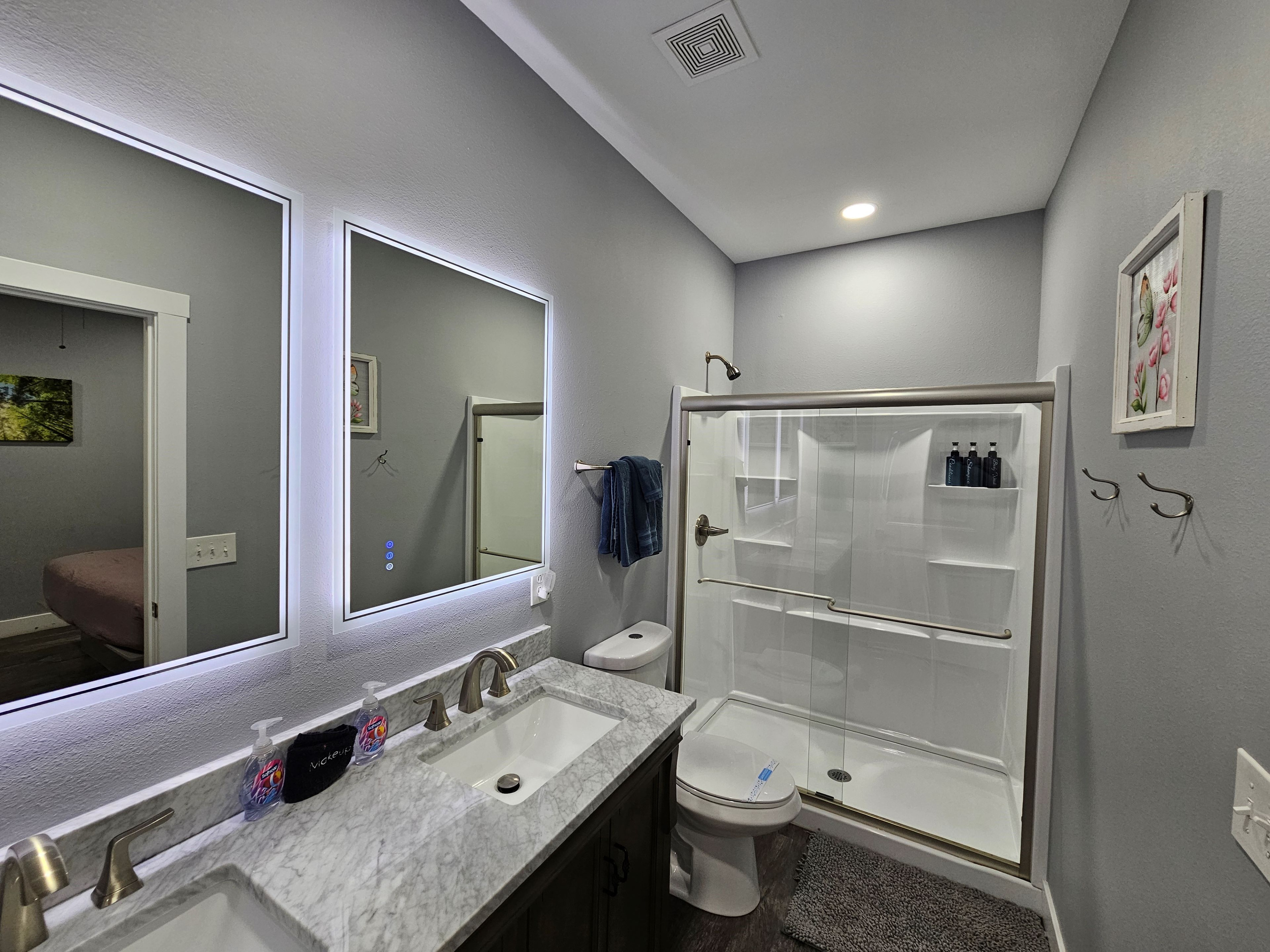 Clean and inviting bathroom with walk in shower, backlit mirrors, & fresh linens