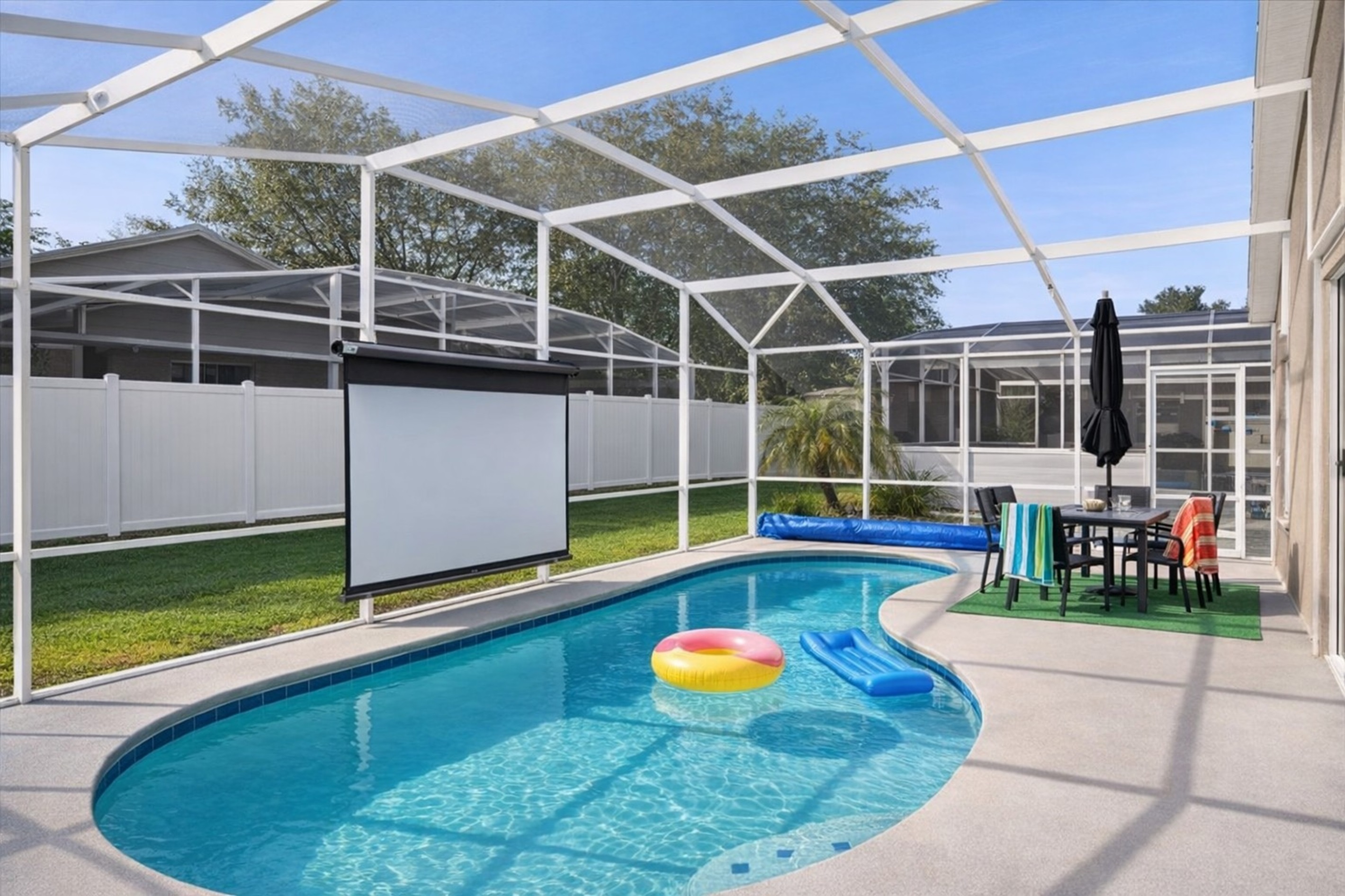 Enjoy a private screened pool area with an outdoor dining space and a projector screen for entertainment.