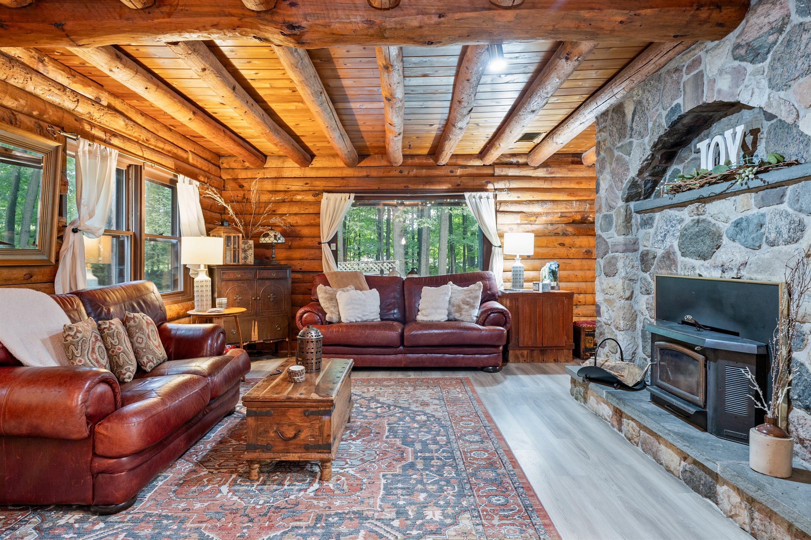 Relax by the stunning stone fireplace in a spacious log cabin living room with leather sofas, natural light, and timeless lodge décor.