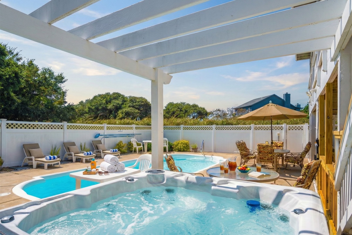 The relaxing poolside patio area complete with a bubbling hot tub, a white pergola for shade, and an outdoor table for al fresco dining.