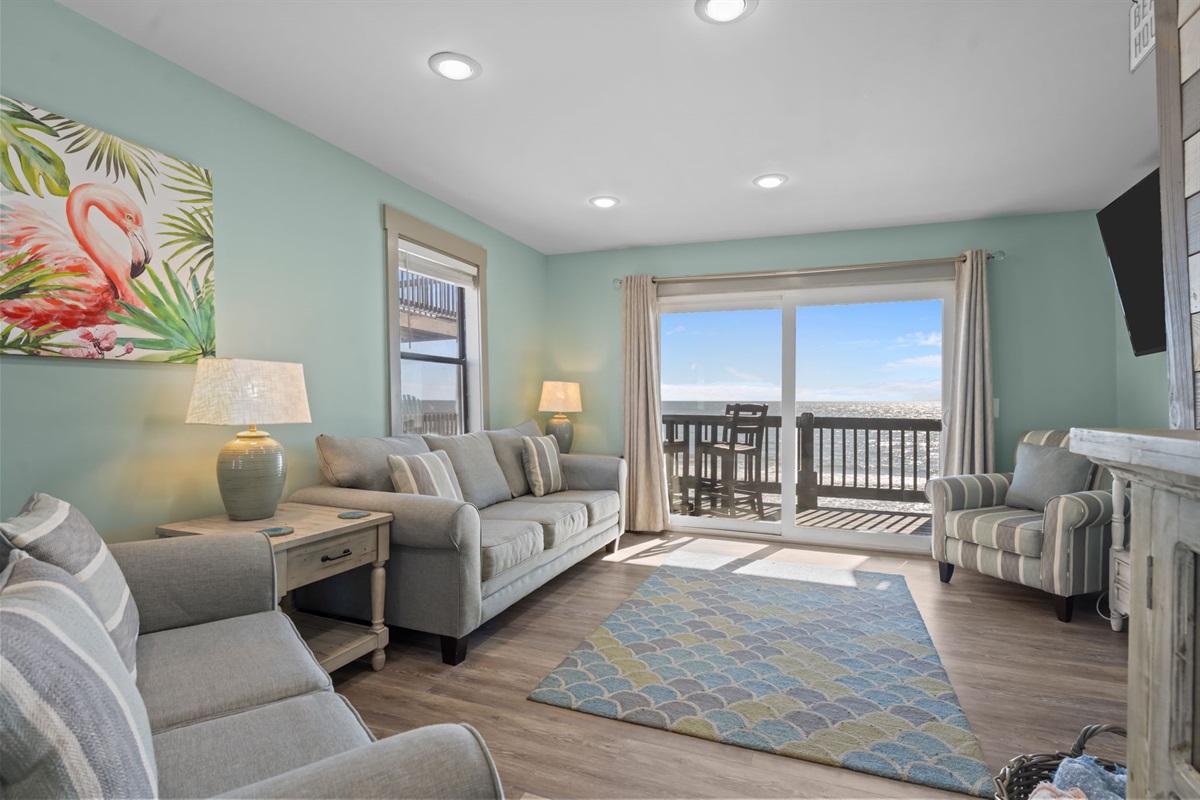 Spacious and inviting living area with plush seating, coastal accents, and floor-to-ceiling sliding doors that frame beautiful ocean views and lead straight to the balcony