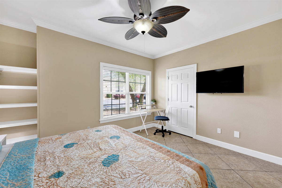Primary bedroom with king bed, ceiling fan, wall mounted smart TV and en-suite bathroom 