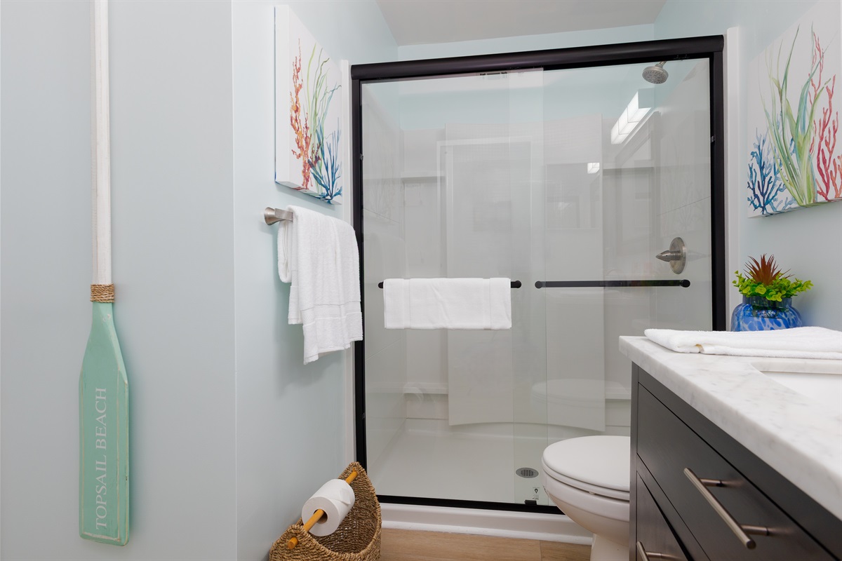 Incorporates a glass shower, a vanity with ample storage, and a comfortable toilet.