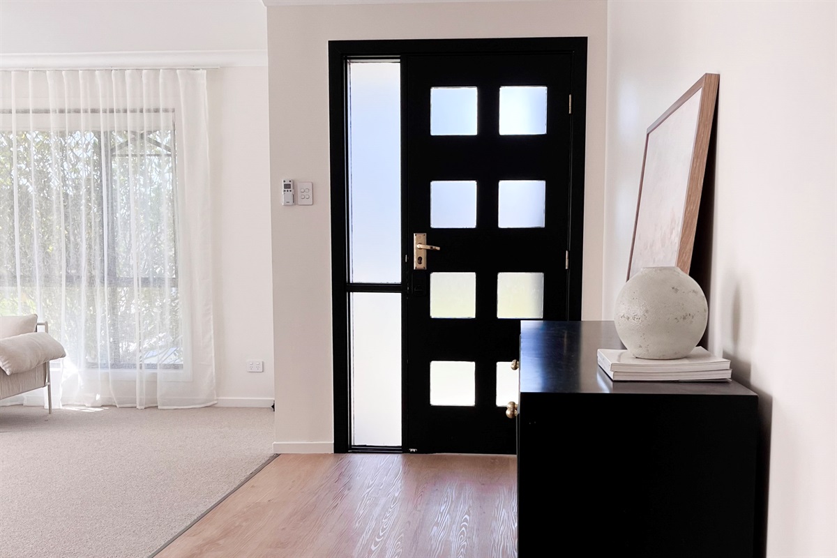 The front entry shows the black door, timber floor and nearby sitting area, setting up the home’s clean indoor flow.