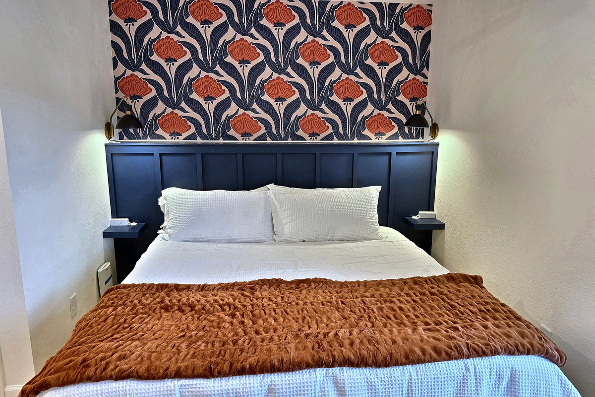 Plush bed with crisp white linens under a bold botanical accent wall