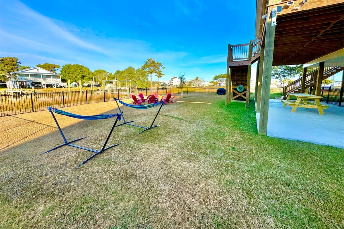 Private backyard dock with boat lift and fillet table, fenced-in backyard, fire pit with Adirondack chairs, hammocks, propane grill, picnic table, outdoor shower, expansive waterfront back deck with table and seating, neighborhood boat ramp and dock