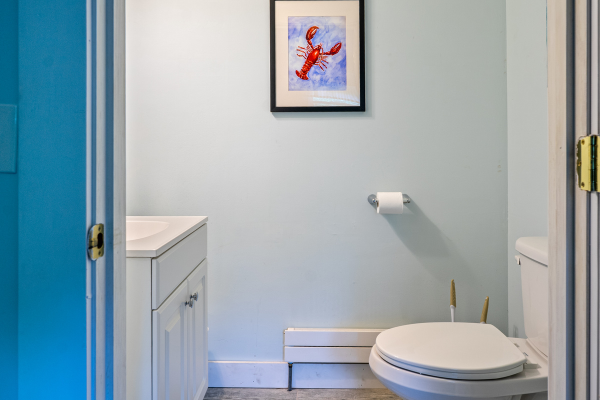 This first-floor half bathroom offers an accessible powder room layout next to the main kitchen area. Complete with a white vanity cabinet and vibrant lobster wall art, this amenity maximizes ground-floor comfort for your Downeast vacation.