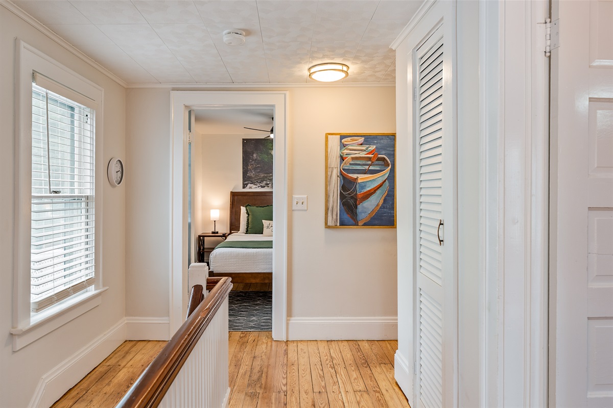 Inviting upper-level hallway with peek into another comfy guest room and colorful wall art.