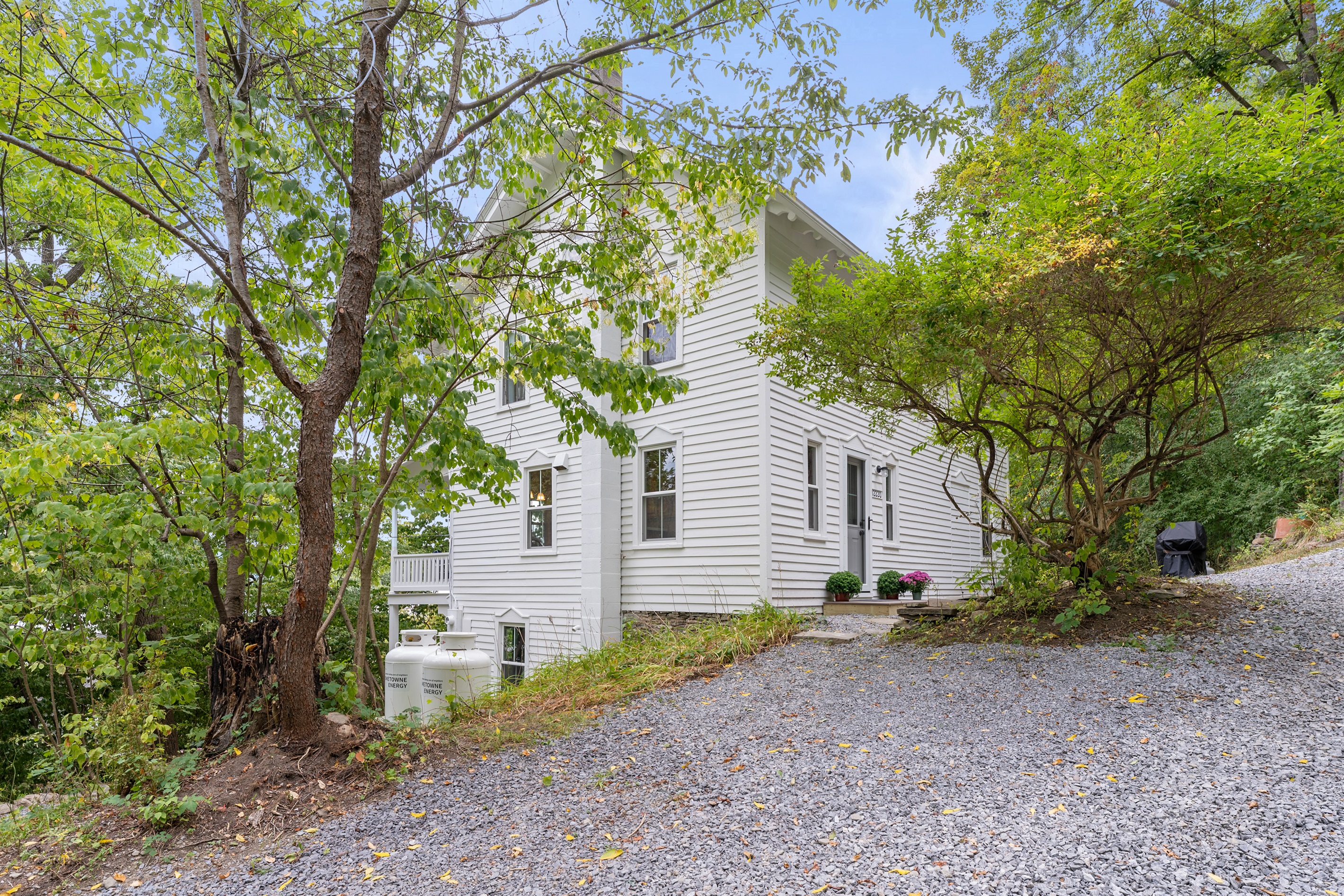 Classic white home nestled among trees with a spacious gravel driveway for easy access.