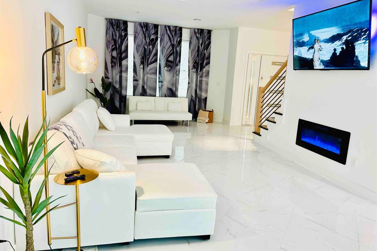 Living room with smart TV and electronic fireplace. Dramatic floor-to-ceiling curtains elevate the vibe while bringing privacy into the home.