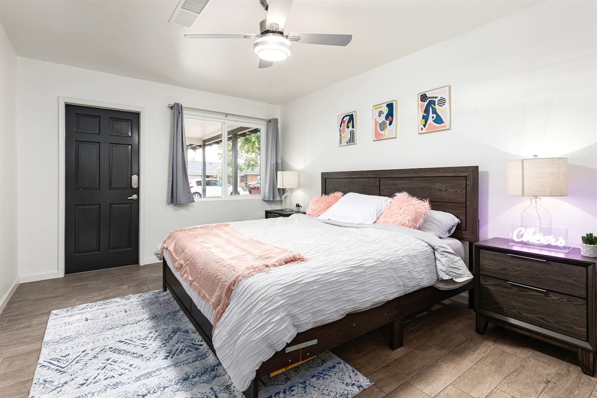 This stylish retreat features a modern king bed, playful wall art, and blush pink accents for a vibrant yet relaxing atmosphere.

