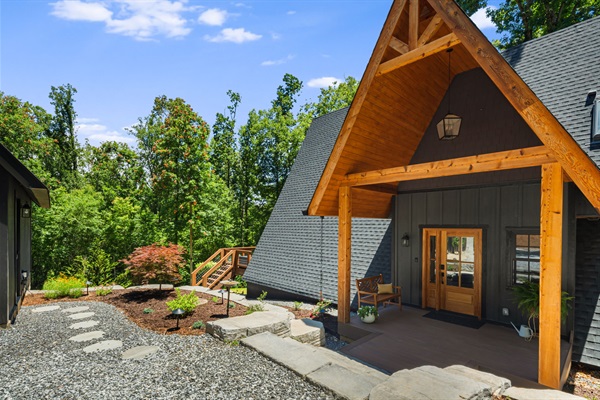 The welcoming front porch is a few steps from the gravel driveway and parking area. Cedar columns frame the entrance and invite you to come in and enjoy this modern A-Frame cabine offering a blend of cozy charm and upscale style in a private setting.