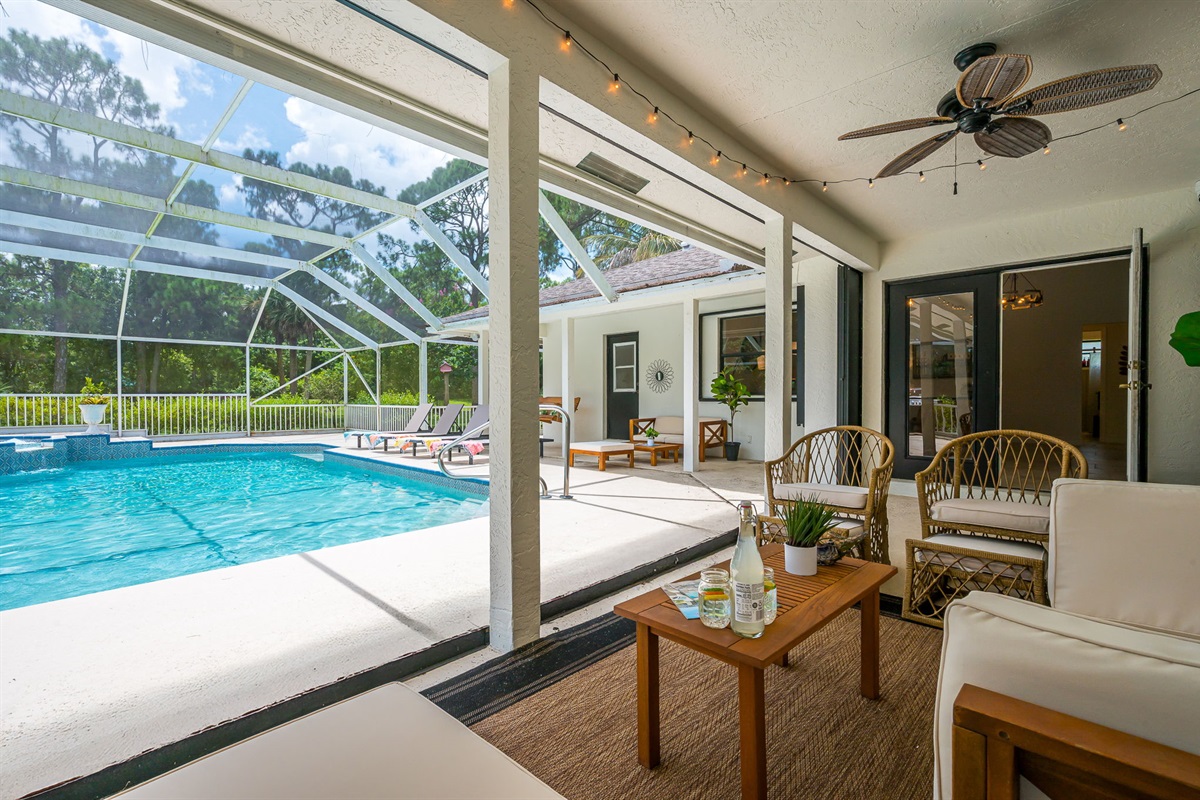 Screened-in pool area with heated pool and spa, surrounded by lush greenery. Features ample lounge seating, BBQ grill, and cozy covered patio with outdoor dining and relaxing sitting area.