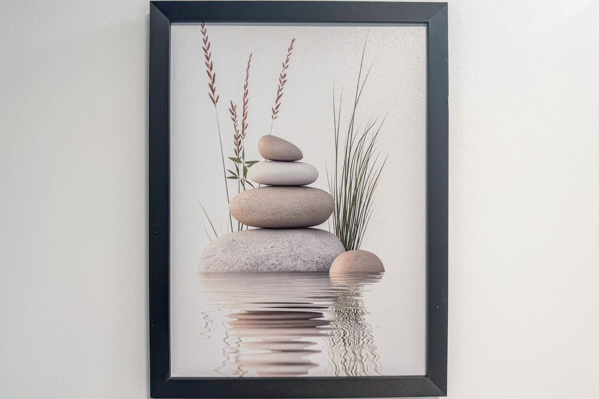 A close-up view details the framed wall art inside the upstairs bathroom, a playful nod to the home's name, "A Stone's Throw." This black-framed print features a balanced stack of zen stones reflecting over calm water against a white wall.