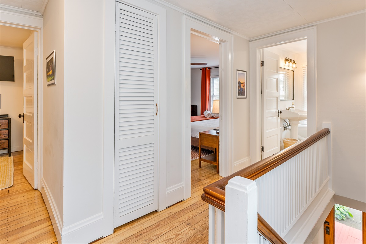 Crisp and clean upper hallway with vintage charm, hardwood floors, and access to bedrooms and full bath.