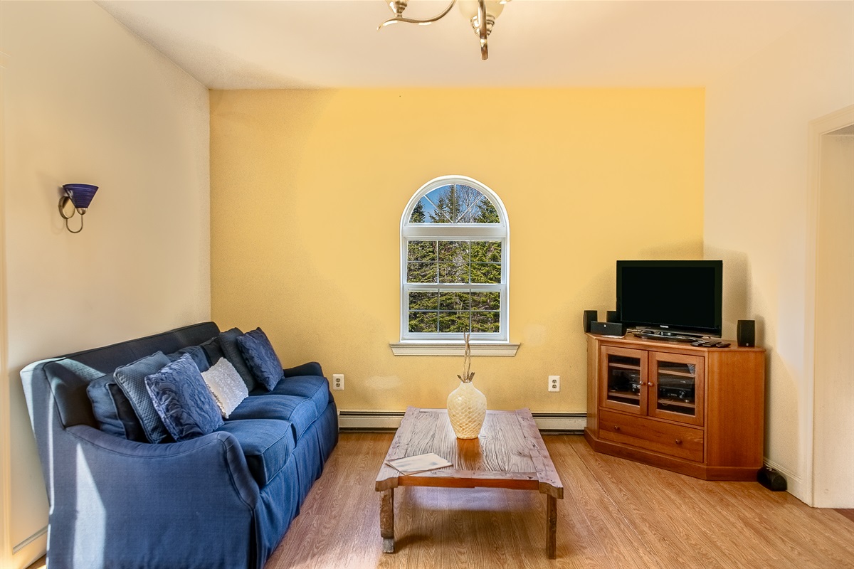 Unwind in the living room, featuring a Roku Smart TV for all your favorite streaming apps. This bright gathering space offers comfortable seating and views of the surrounding woods, perfect for a movie night after exploring Acadia National Park.