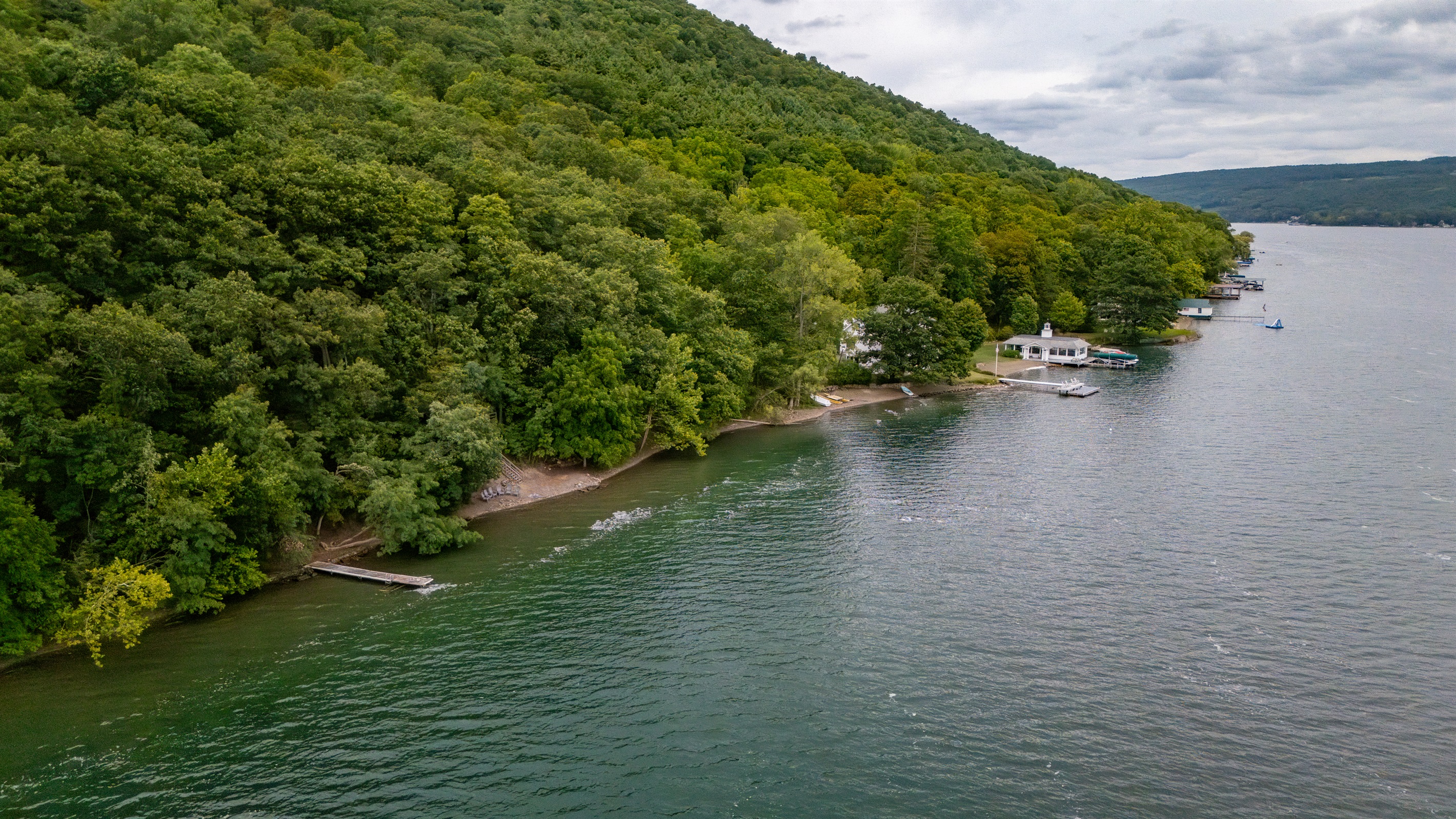 Aerial view of a private, wooded shoreline retreat with direct lake access, dock, and Adirondack chairs for lakeside relaxation.