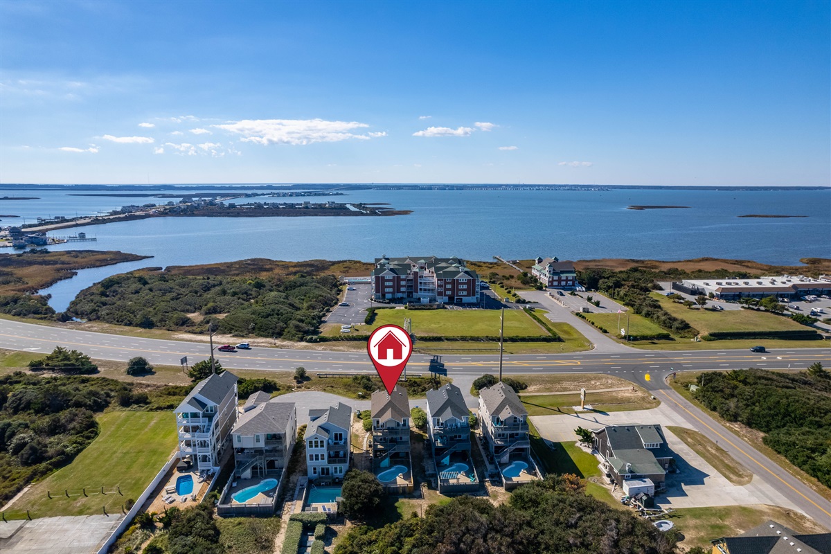 A sweeping drone shot capturing the neighborhood’s peaceful setting, with the home marked and surrounded by soundside views and open green areas.