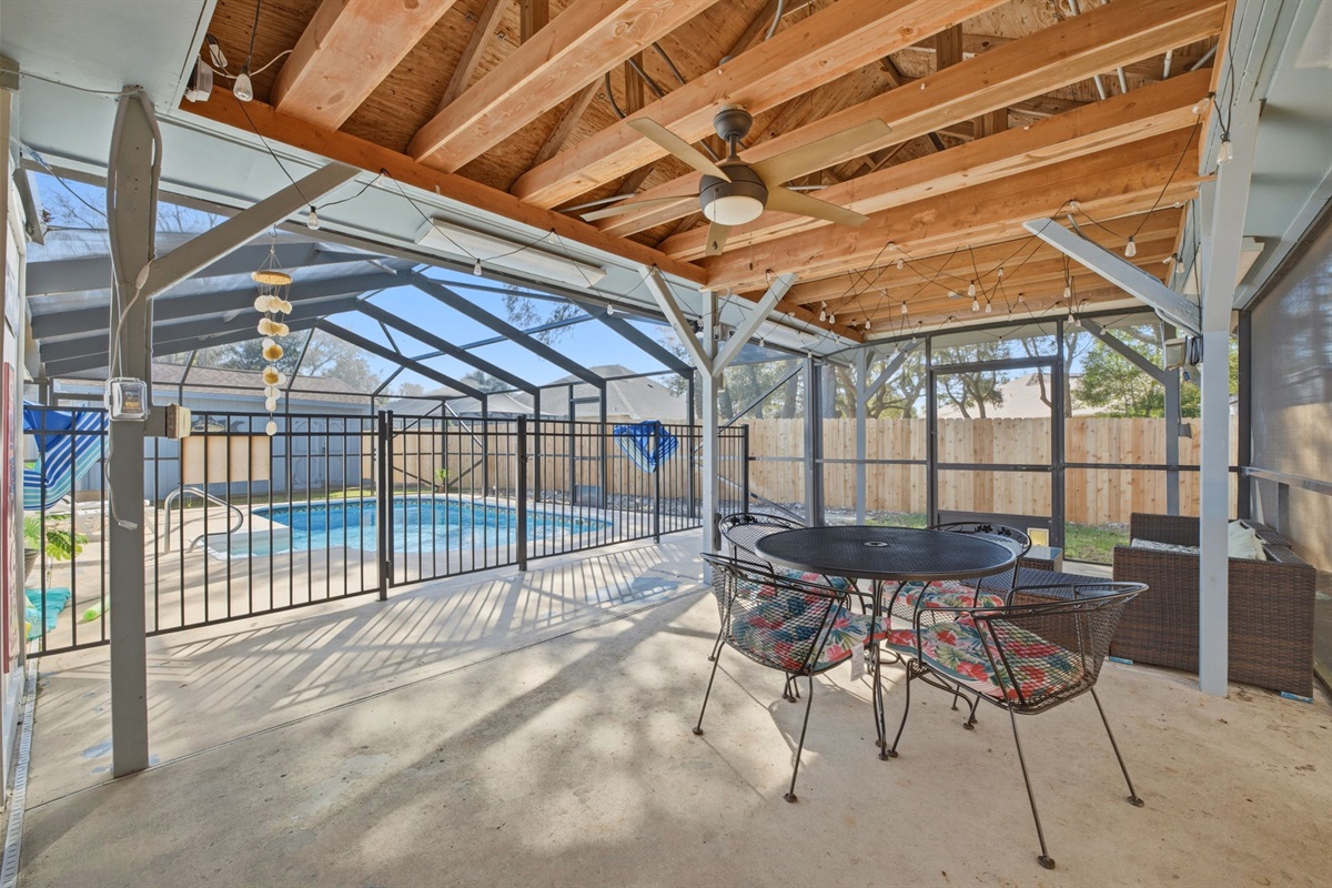 Enjoy year-round outdoor living in this spacious covered patio featuring beautiful exposed wood beams, ceiling fans, and charming string lights. The screened enclosure overlooks a sparkling pool, creating the perfect setting for relaxing afternoons.