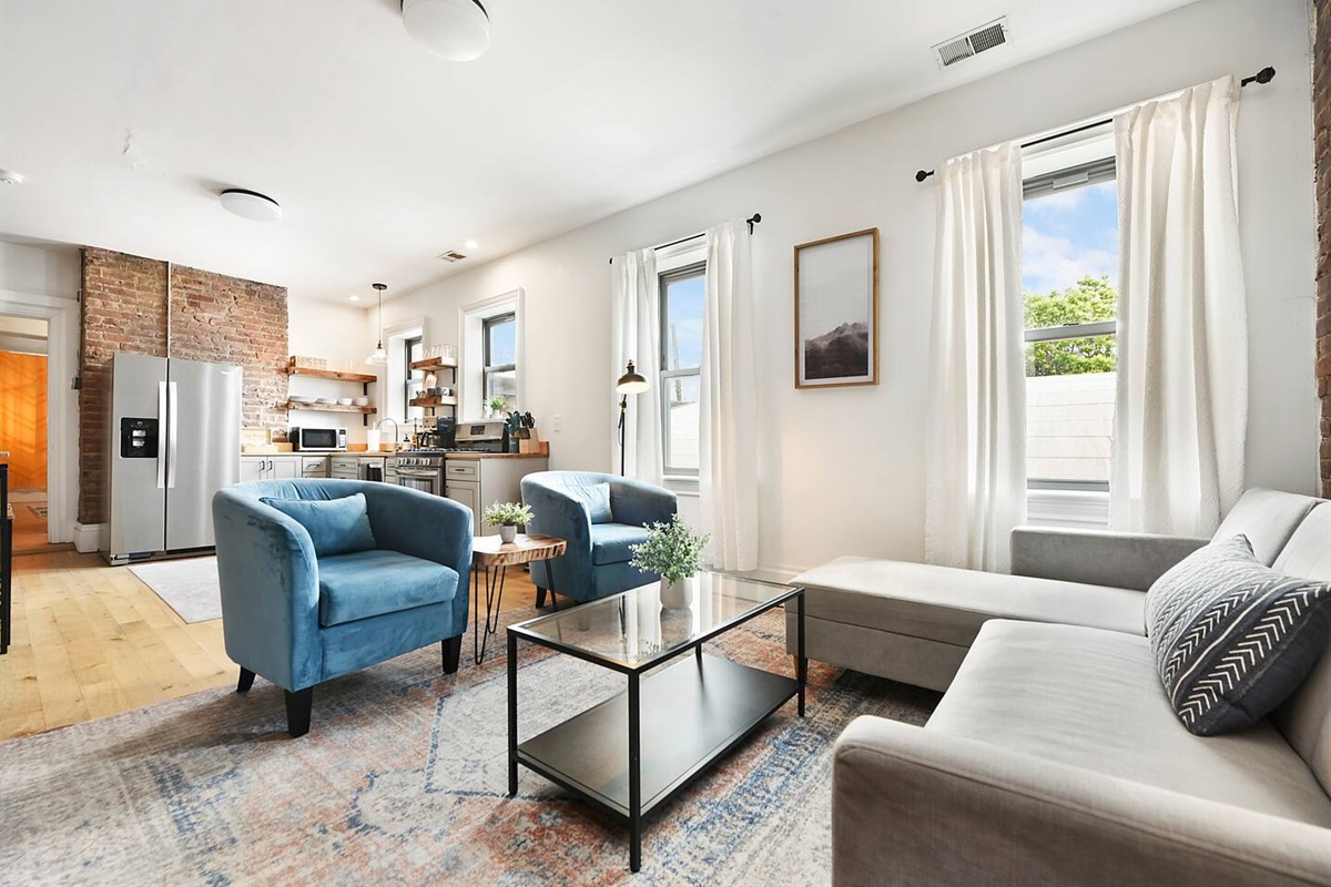 This vibrant living space features an L-shaped sofa, a sleek coffee table, cozy chairs, and a stunning brick wall with natural light pouring in.
