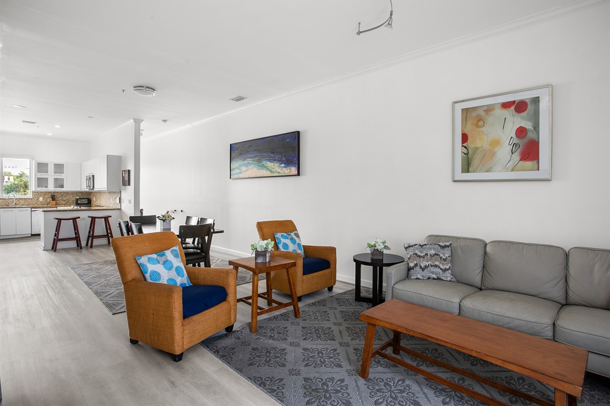 Living room with leather sofa, accent chairs, and a 50-inch flat screen TV. Sliding glass doors open to a Juliet balcony for sea breeze.