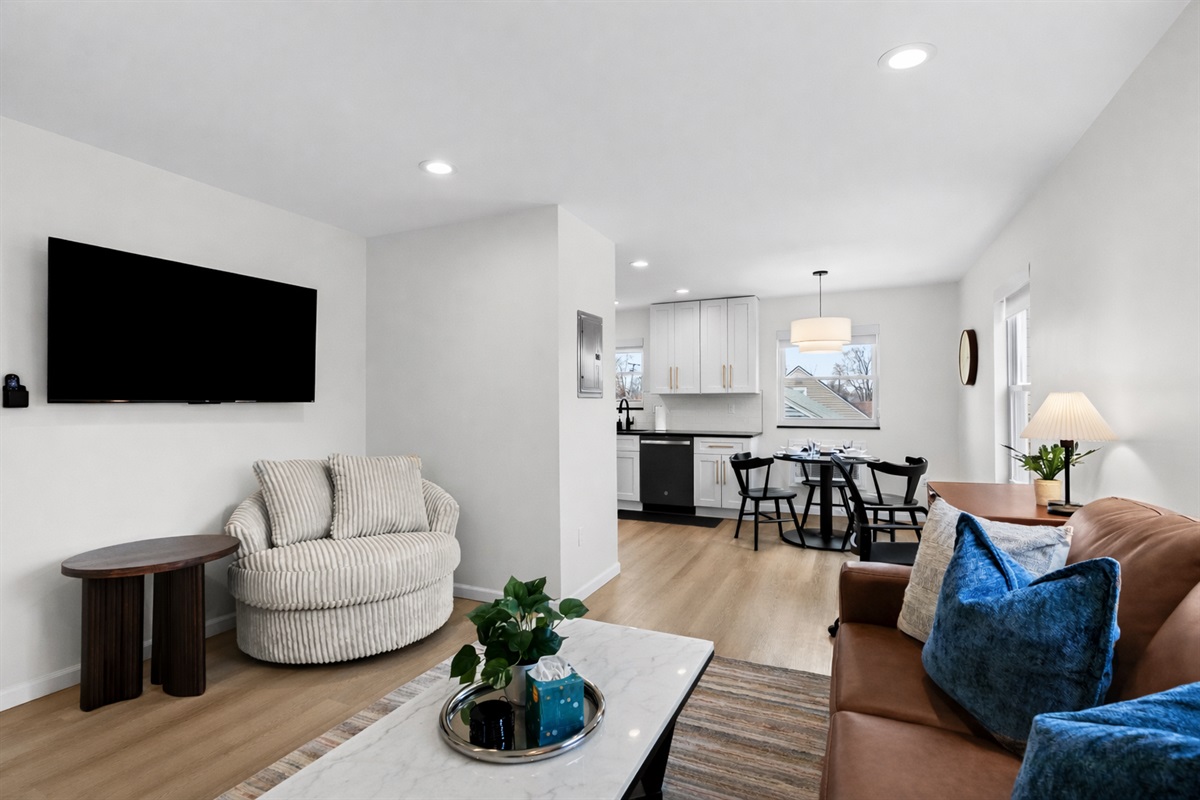 Open-concept living space with modern seating, smart TV, and seamless flow into the kitchen and dining area—bright, airy, and designed for comfort and connection.