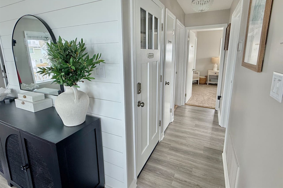 You are welcomed by a bright and charming hallway, featuring crisp white shiplap walls and an elegant black console table that sets a stylish tone for the rest of this inviting coastal home.