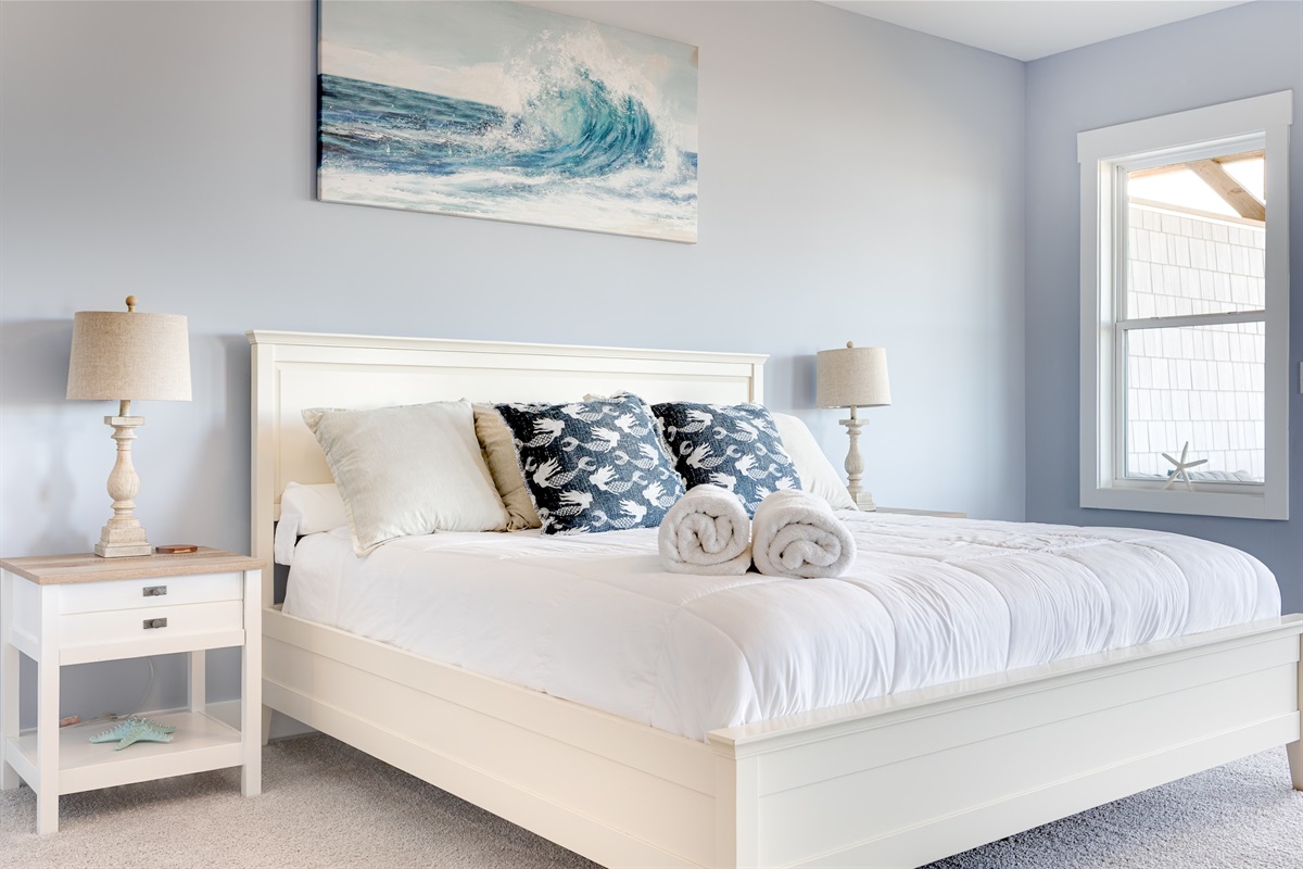 Crisp white linens, plush pillows, and ocean-inspired artwork set the tone for a relaxing stay in the Master bedroom