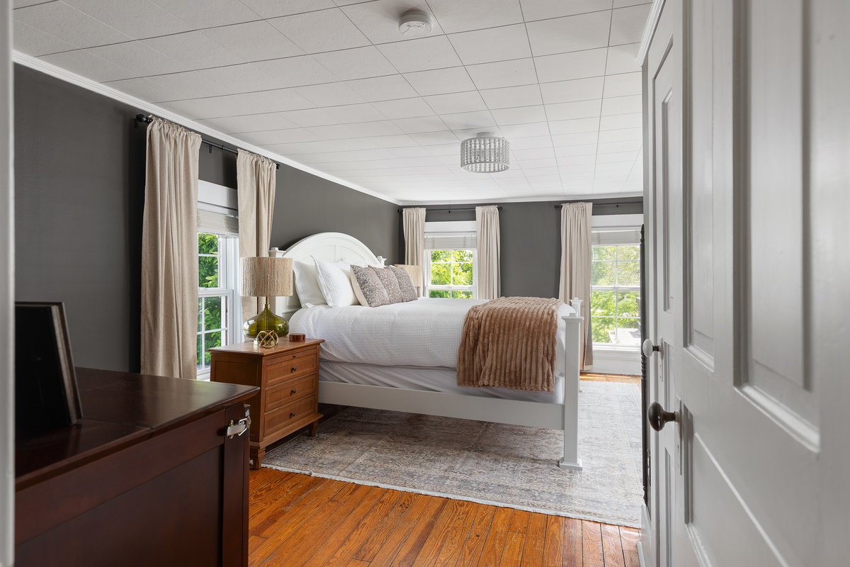 Relax in this cozy, moody retreat featuring crisp white bedding, warm wood floors, and soft neutral tones. A peaceful space to unwind that was designed to feel both elevated and inviting.