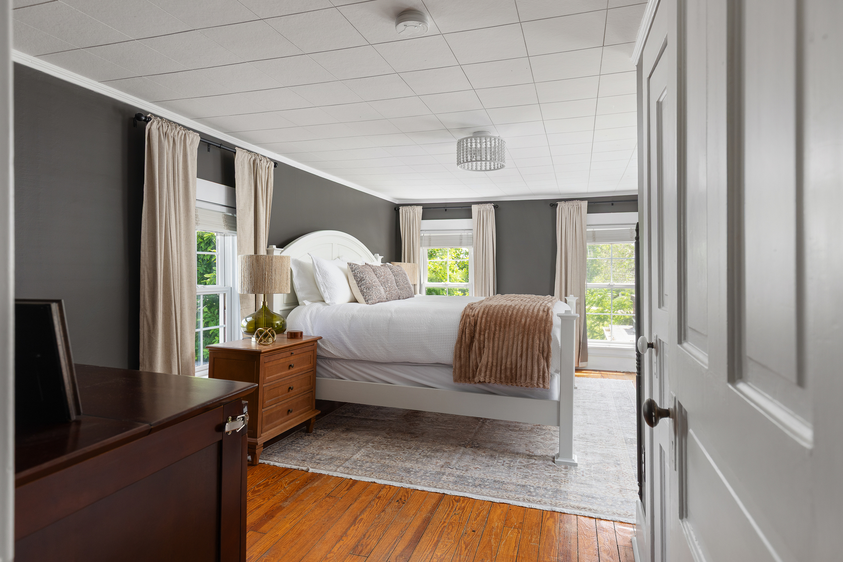 Relax in this cozy, moody retreat featuring crisp white bedding, warm wood floors, and soft neutral tones. A peaceful space to unwind that was designed to feel both elevated and inviting.