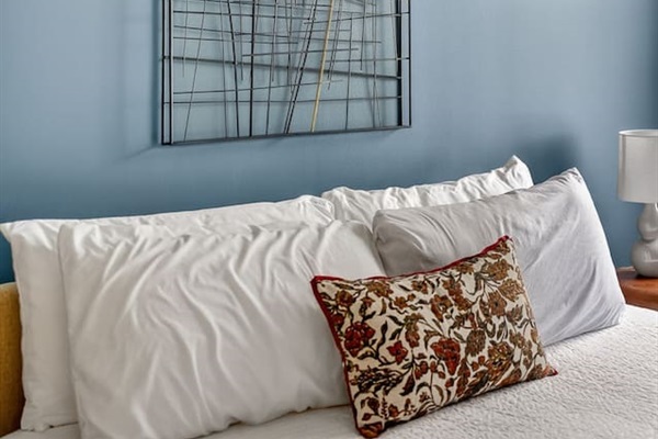 Wake up surrounded by modern design. This bedroom blends soft white linens, a calming blue accent wall, and artistic décor—an oasis of style and tranquility in the heart of the city.