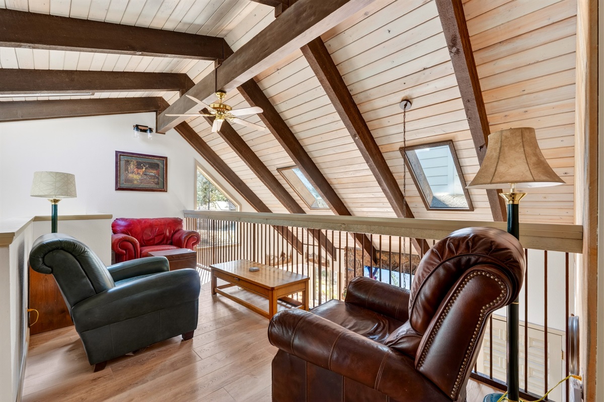 Upstairs, a cozy reading corner features comfortable seating and a bookshelf, overlooking the living room below—an inviting spot to unwind with a book or enjoy a quiet moment.
