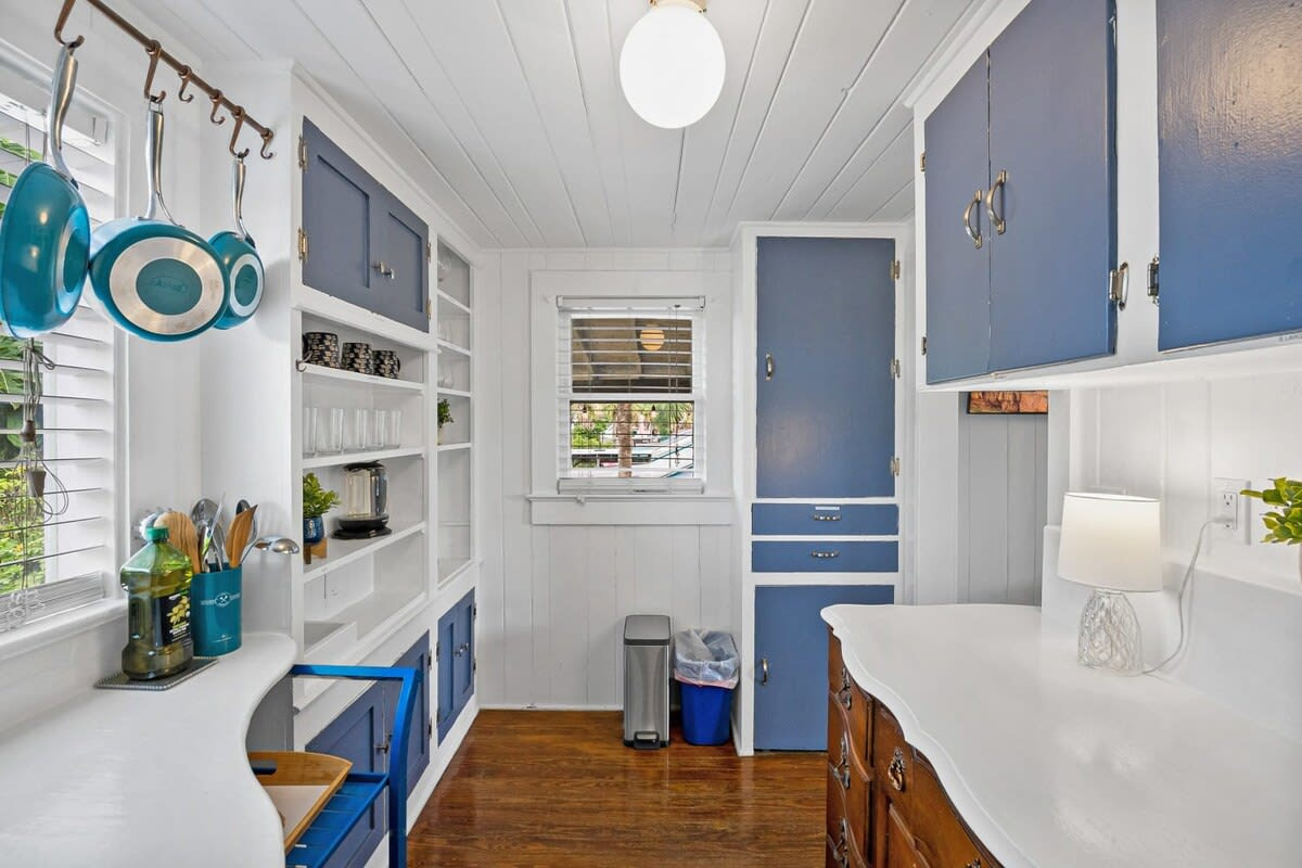 The galley kitchen is small, characterful and blue: pans hanging on the rail, wine glasses on the shelf, everything where you can see it. There is no dishwasher here, so it is hands in the sink and somebody on drying.