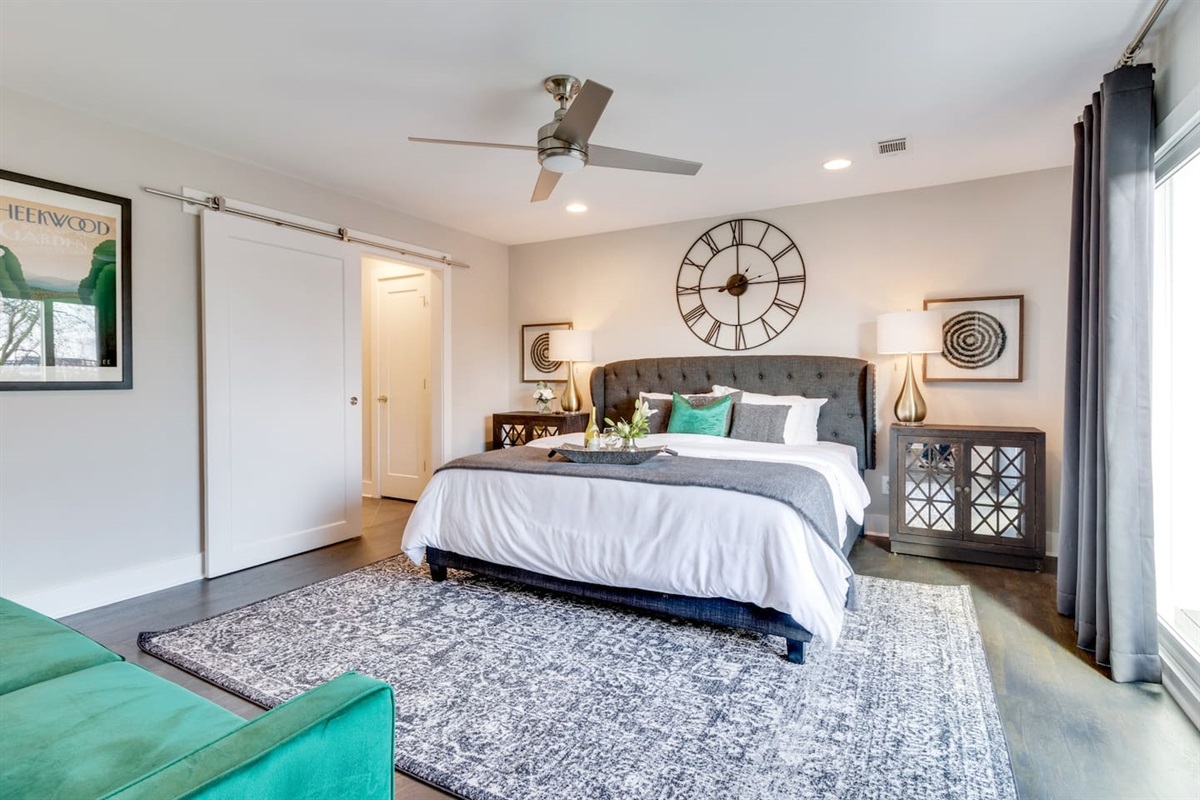 - King size bed with a tufted headboard and bold decor pieces create a stylish retreat - Sliding barn door offers access to a private ensuite, adding rustic modern flair - Neutral tones are balanced by warm lighting and classic mirrored nightstands