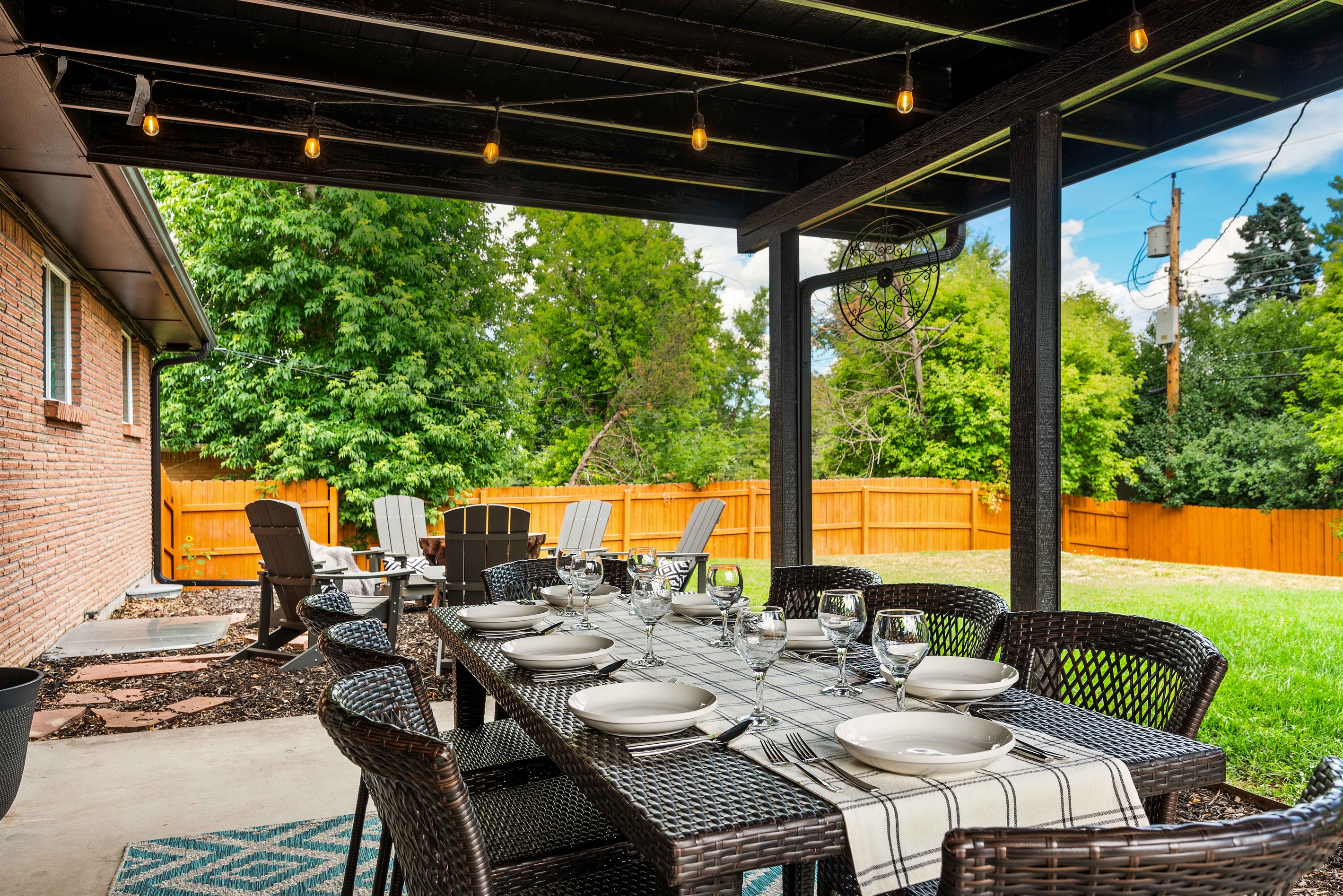Covered patio with a large dining table, string lights, and comfy seating. Steps from the fire pit and fully fenced yard—perfect for meals, coffee, and relaxing outdoors.