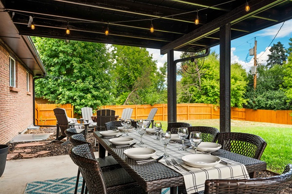 Covered patio with a large dining table, string lights, and comfy seating. Steps from the fire pit and fully fenced yard—perfect for meals, coffee, and relaxing outdoors.