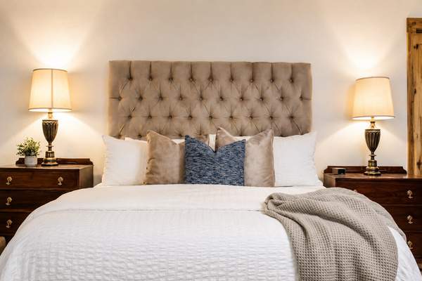 Retreat to the spacious primary bedroom, designed for a restful night after a day on the lake. Crisp bedding, a plush upholstered headboard, layered pillows, and warm bedside lighting create a comfortable, inviting space with a polished lake-house feel.