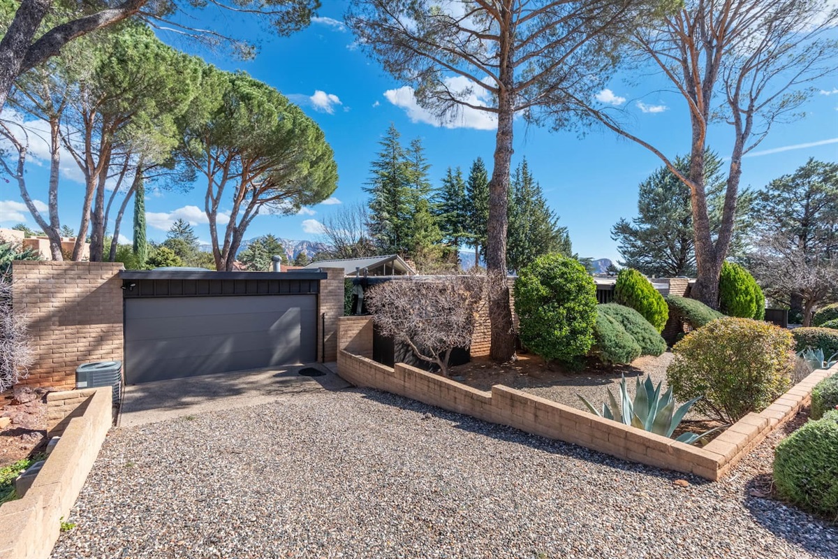 Private driveway entrance with modern garage, mature trees, and thoughtfully designed terraced landscaping.