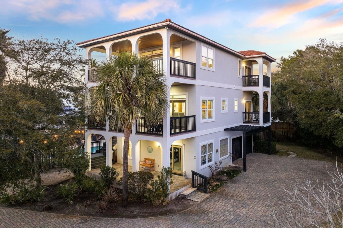 Welcome to The Copper Fin! Grand front view highlighting custom arched balconies, extensive paver parking, and a lush coastal setting.