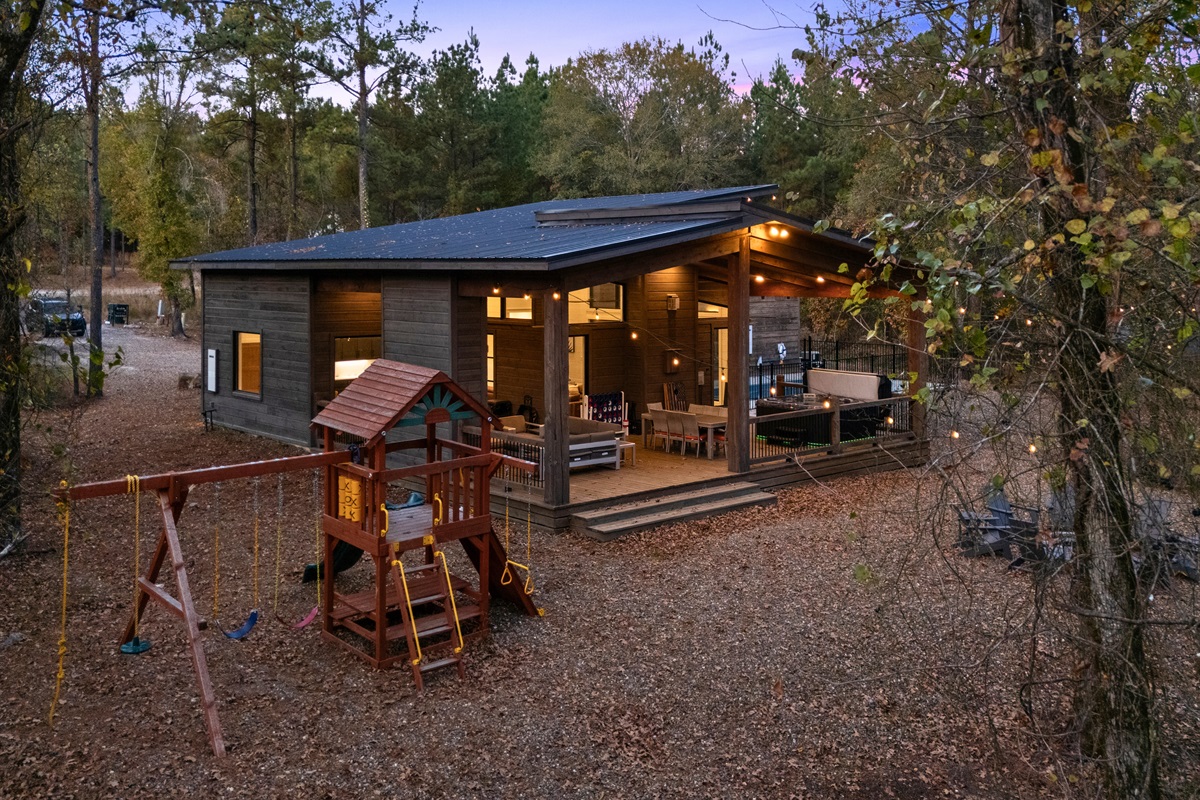 A wide view of the cabin shows just how much room there is to play, relax, and explore, with a private playground and a welcoming outdoor space tucked right into the woods.
