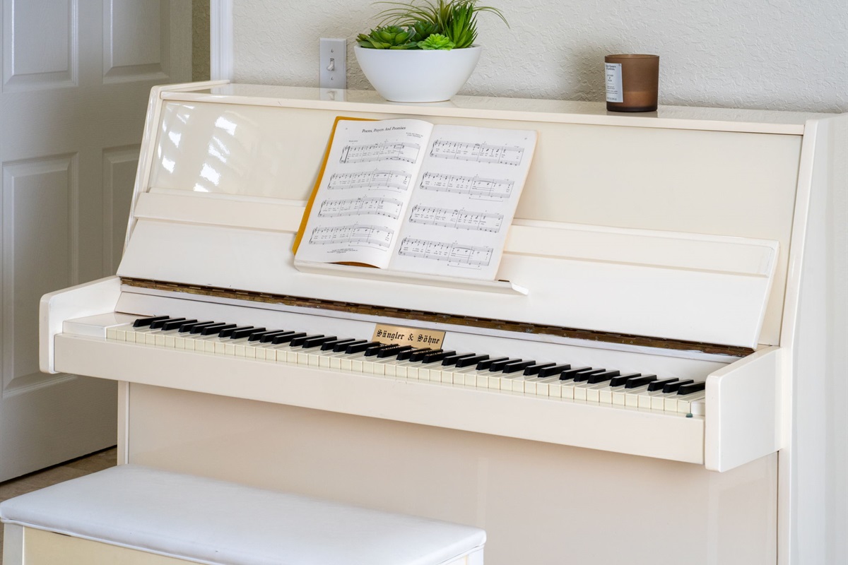 A sleek ivory upright piano with an open music book, topped with a potted plant and candle for a touch of charm.