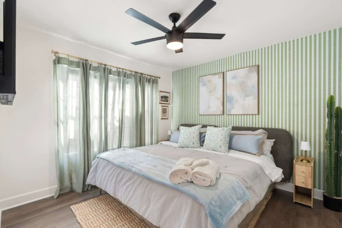 Bright guest bedroom with green striped accent wall, soft linens, and natural light—a calming retreat with thoughtful style.