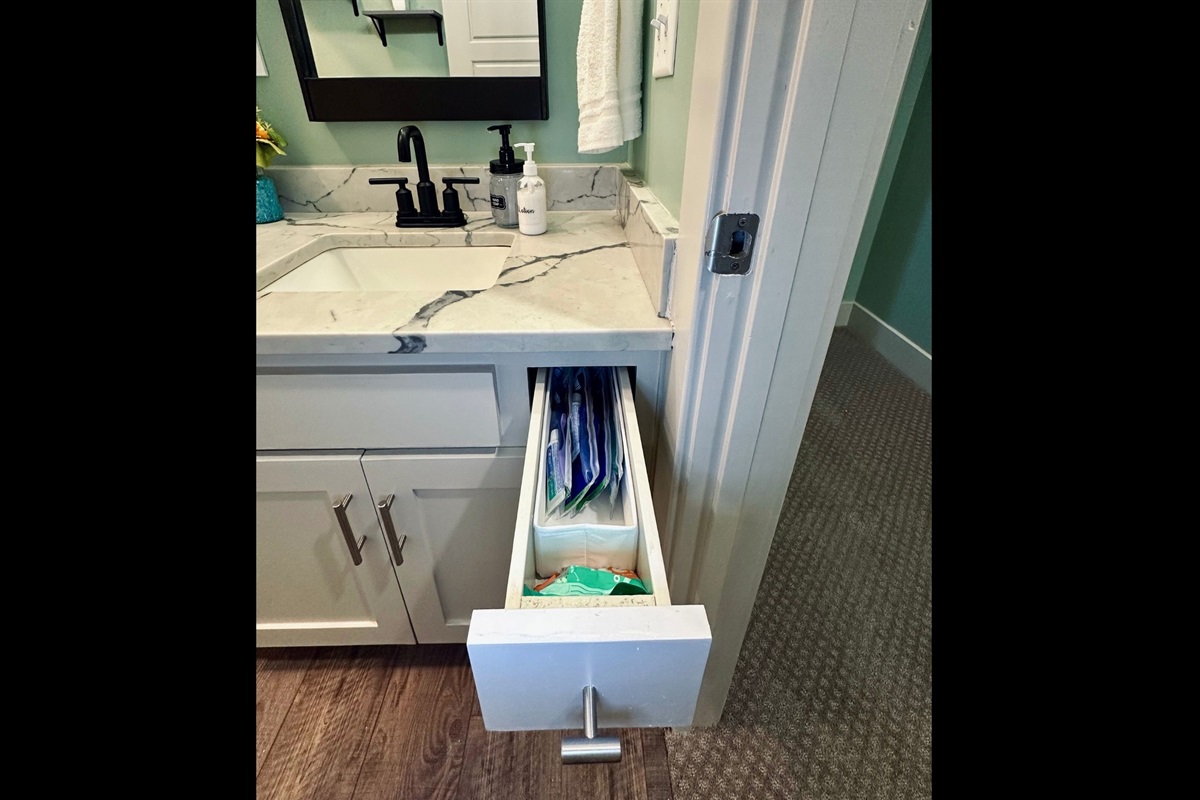 Hall bathroom vanity drawer stocked with toothbrushes, toothpaste, and floss for practical daily needs.