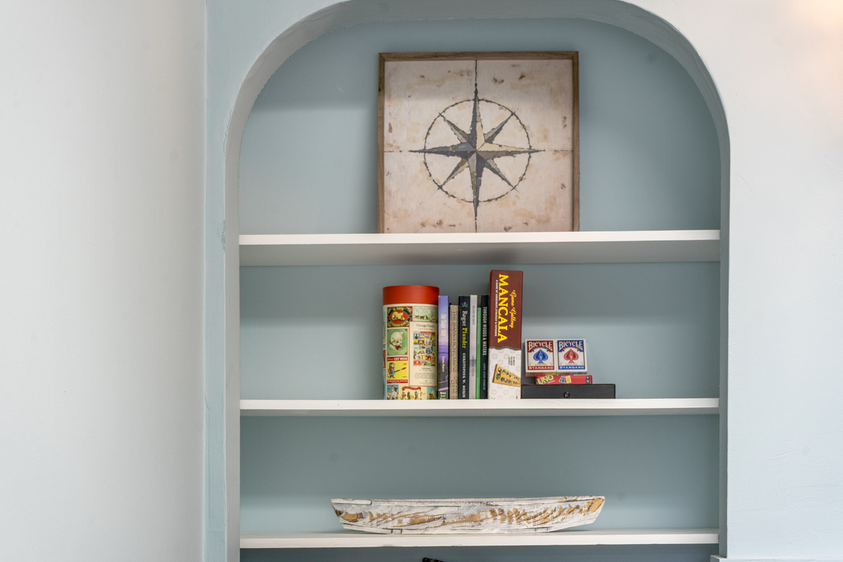 Gather the family for a fun game night. This close-up highlights the den’s built-in collection of classic books, puzzles, and board games like Mancala, Uno, and playing cards, all stored neatly under the room’s namesake compass rose artwork.